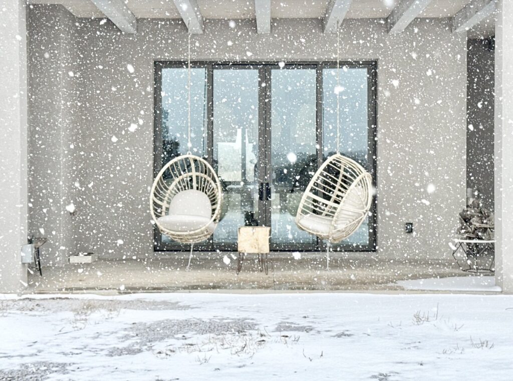 A white house surrounded by snow features two chairs and a table, embodying a serene winter scene in a festive setting.