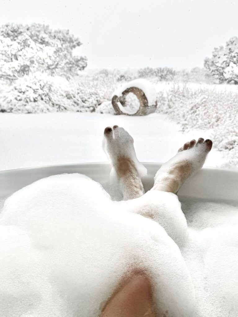 A pair of feet in a snow-filled bathtub, capturing a cozy and imaginative winter scene that invites relaxation and wonder.