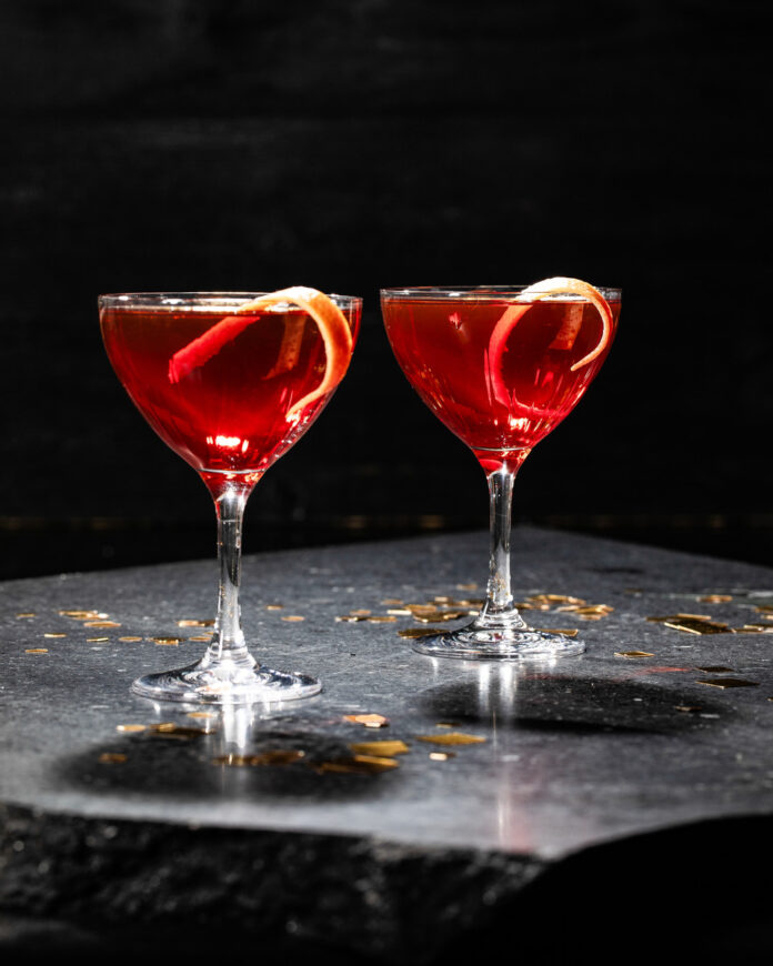 Two elegant glasses of red wine garnished with a twist of grapefruit, set against a cozy indoor backdrop.