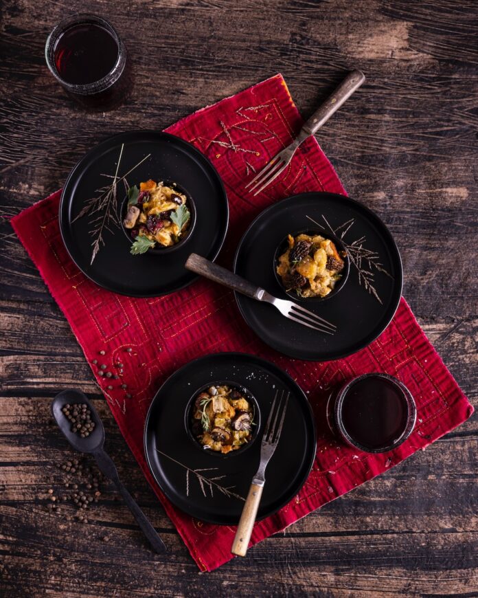 Three black bowls hold three servings of stuffing with forks inside each bowl and a red cloth below the bowls.