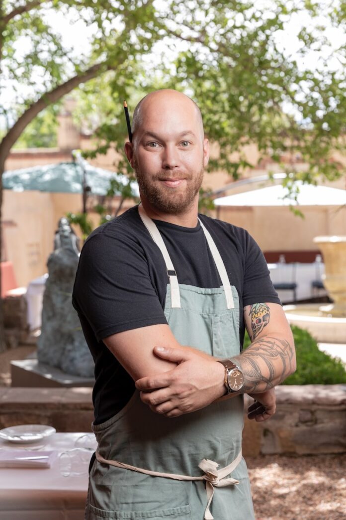 Chef Weston Ludeke of The Compound in his apron stands in a brightly lit courtyard