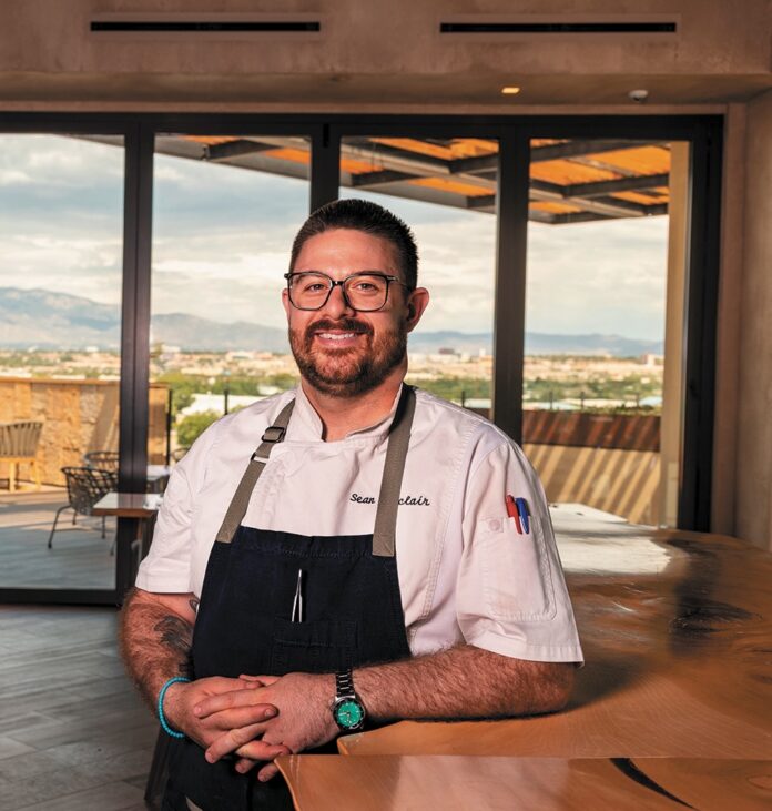 Chef Sean Sinclair stands in his restaurant in Albequerque, smiling at the camera
