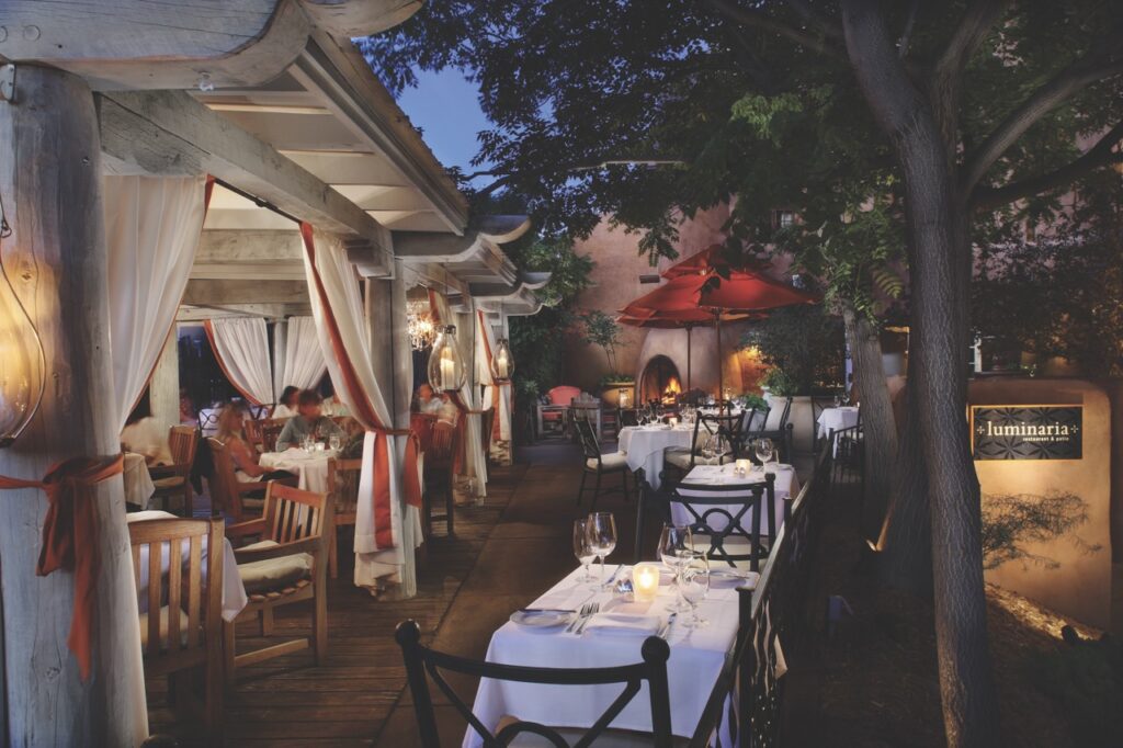 Various white tableclothed tables sit outside beside a white tent and red umbrellas at Heritage Hotels.