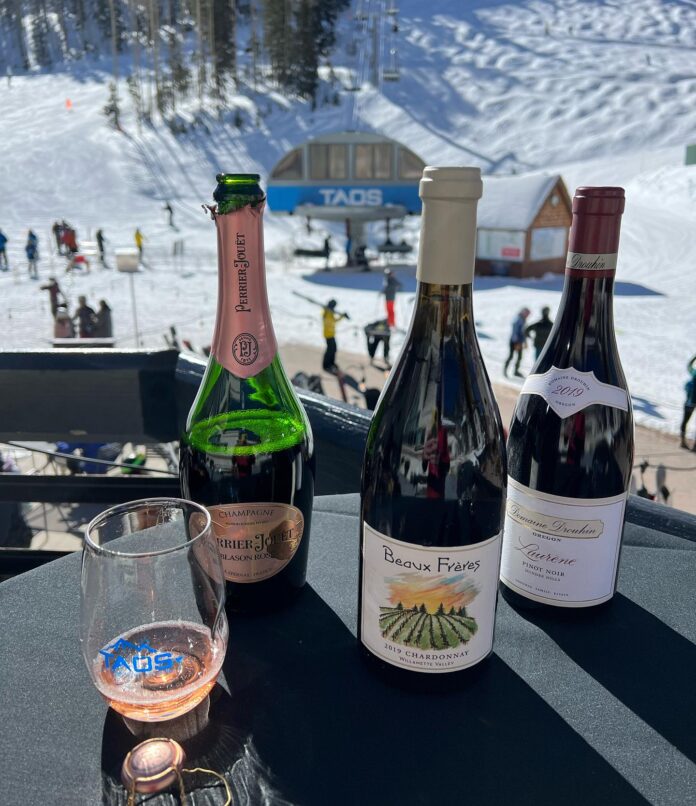 Three bottles of wine sit on a table over looking the snow at the Taos Winter Winter Festival.