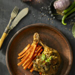 Plated braised duck leg in green chiles and roasted cumin carrot strips topped with parsley.