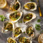 Grilled oysters displayed with a cilantro topping on a wooden table.
