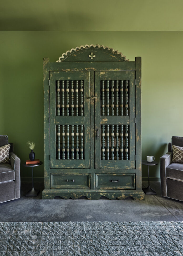 A vintage green wooden cabinet with intricate spindle detailing and a distressed finish, set against a muted green wall.