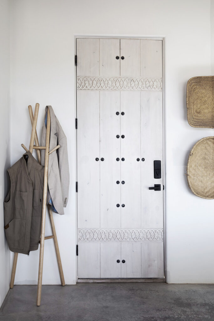 Minimalist entryway with a white wooden door featuring intricate carvings, black hardware, and a modern digital lock.