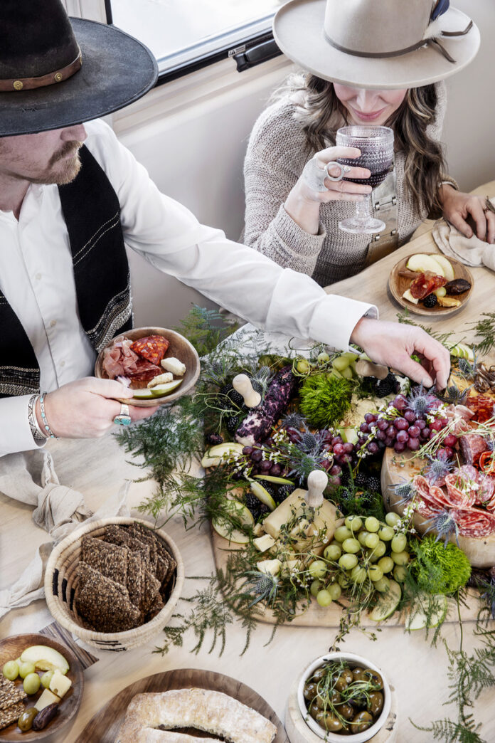 A stylish Santa Fe-inspired charcuterie spread with two people in Western hats enjoying wine and artisanal food, embodying Southwestern hospitality and design.