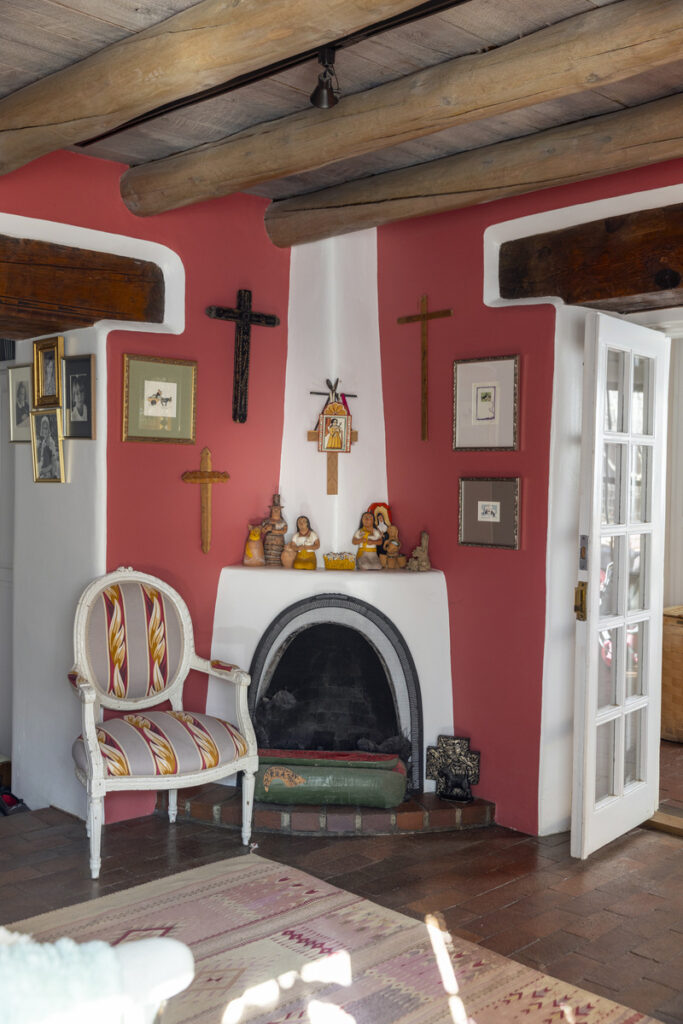 A living room with a traditional kiva fireplace, folk art collection, and rustic wooden ceiling beams.