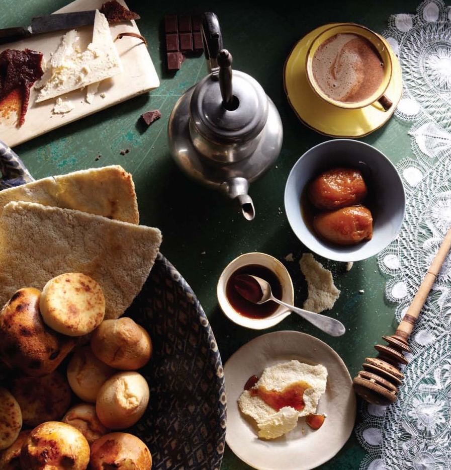 Various small bowls of treats and pastries sit around a pot of hot chocolate and a cup of coffee.