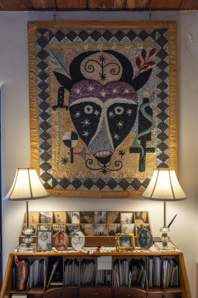 Southwestern home decor featuring a beaded folk art tapestry with a stylized bull motif, a vintage wooden desk with framed family photos, and two classic table lamps.