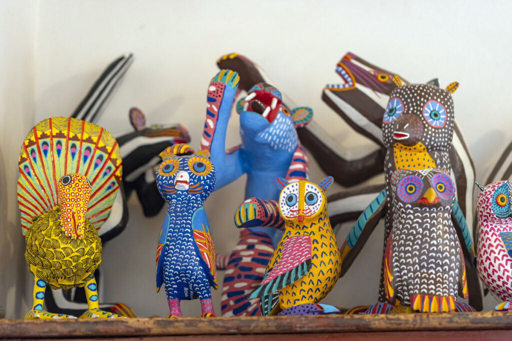 Colorful Mexican folk art animal figurines, including owls, a turkey, and a jaguar, intricately hand-painted with vibrant patterns and designs.