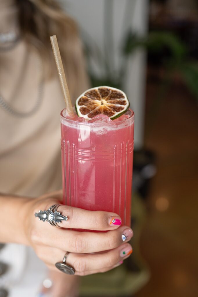 A person holds a pinkish purple drink with a straw and a brulee lemon slice on top.