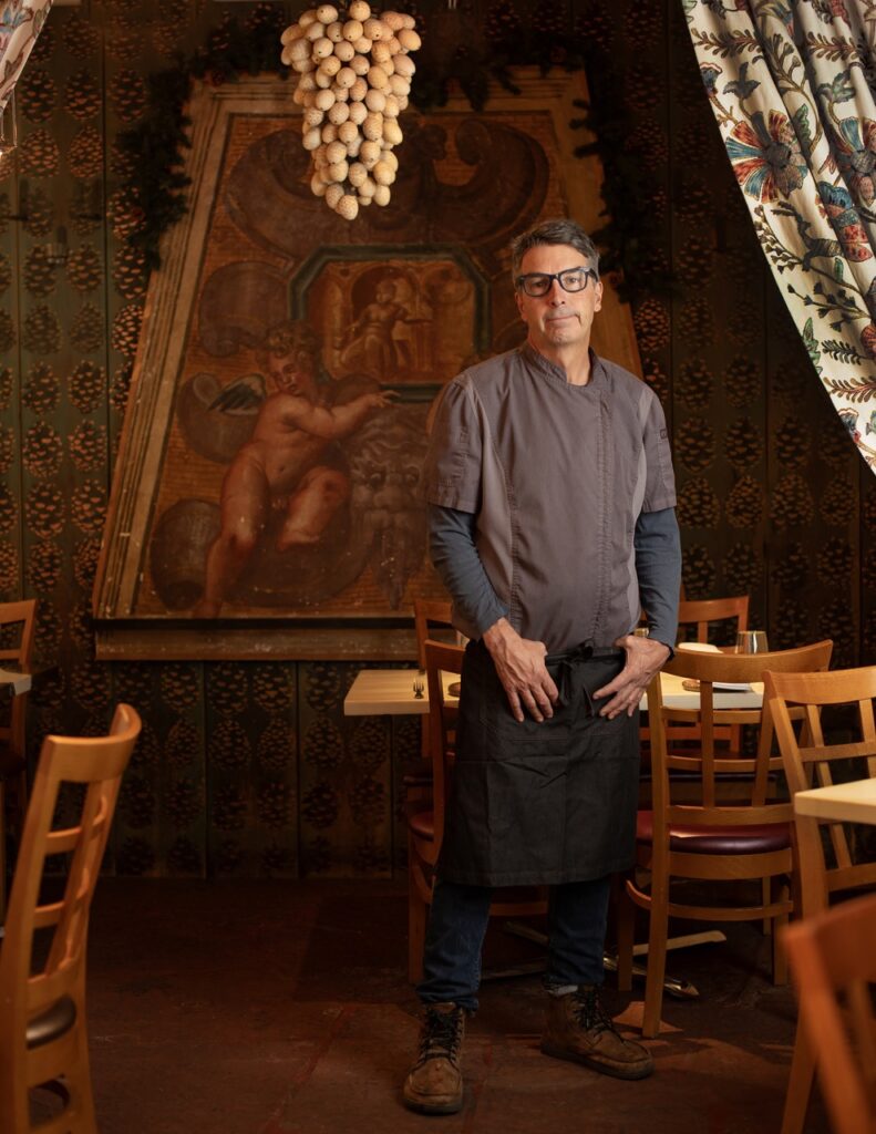 A man stands in the interior of a Santa Fe restaurant with dark walls and drapes throughout. 