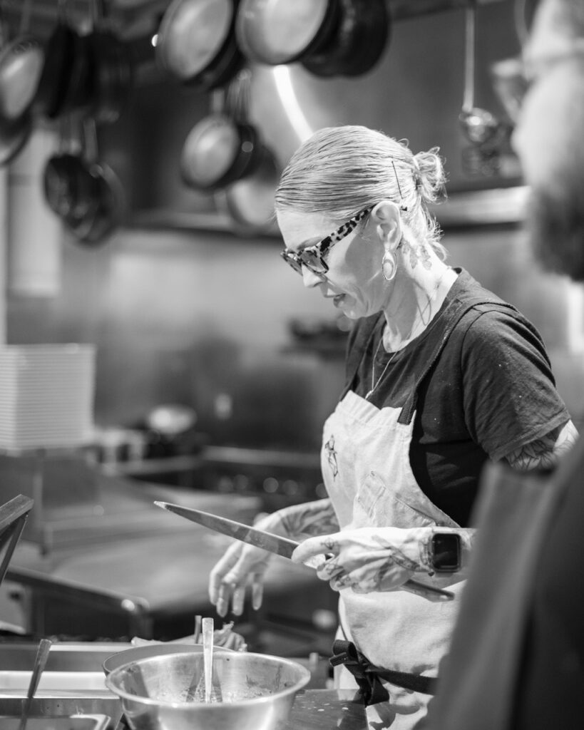 A woman chef at a Santa Fe restaurant zesting an ingredient over a pot in black and white.