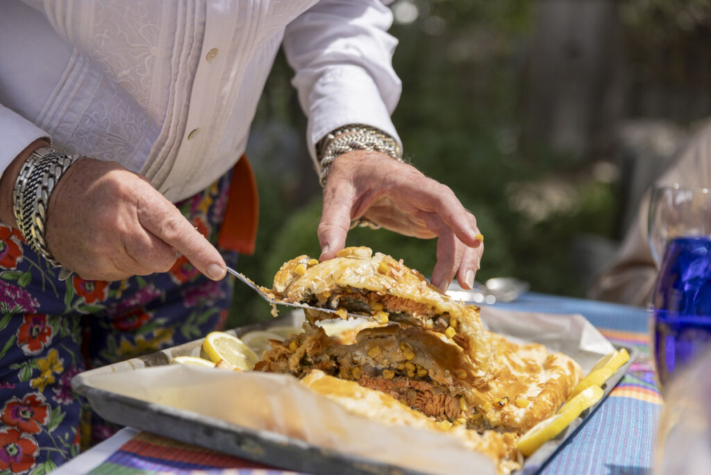 A person in a white shirt is cutting into a layered dish, possibly a pastry or sandwich, filled with meat and vegetables.