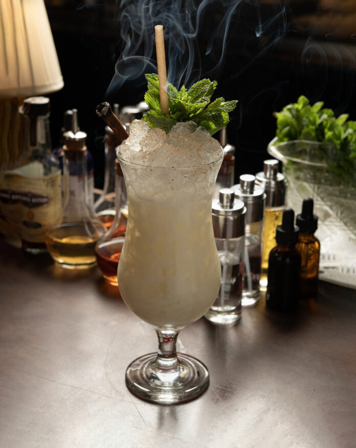 A smoky craft cocktail garnished with fresh mint and a cinnamon stick at a stylish bar in Santa Fe, showcasing the city's evolving eat and drink culture.