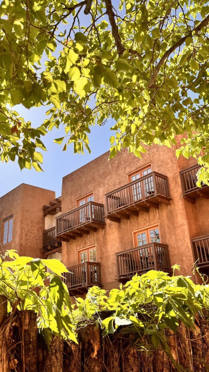 The outside of the Hotel Santa Fe with balconies and windows peaking through green trees.