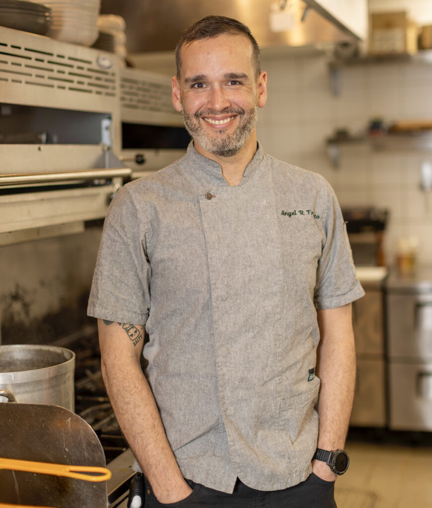 Chef Angel Franco in the kitchen at Palace, showcasing his culinary expertise with a warm smile and professional chef attire.