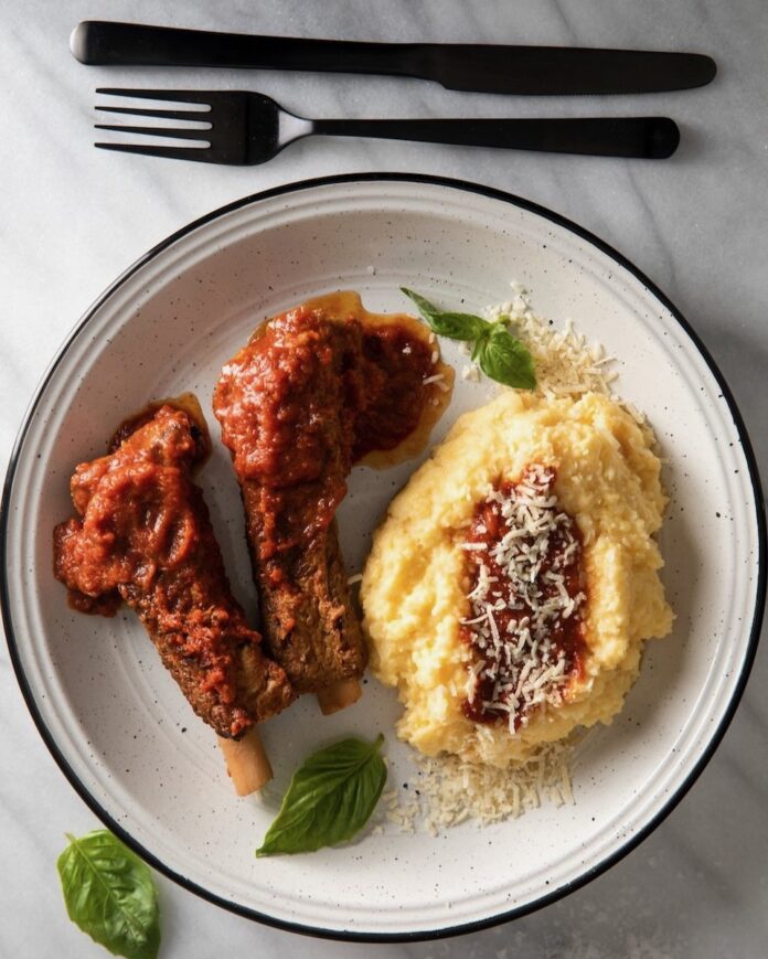 Costole a La Mamma Con Polenta Costole on a white plate with polenta on the side.