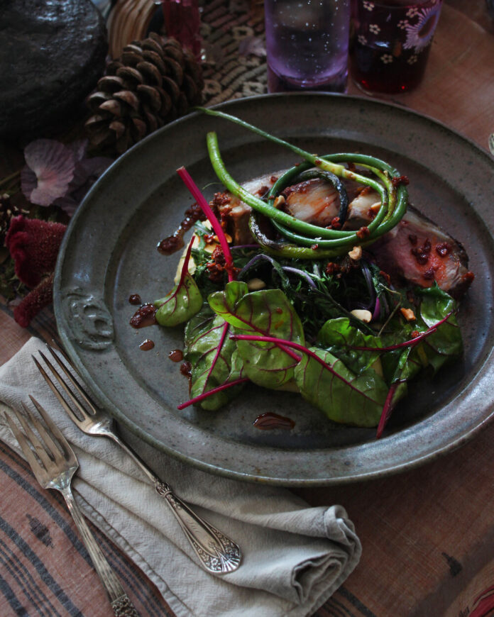 A black plate with a Lamb Rendang on top featuring sauteed greens all on a brown table.