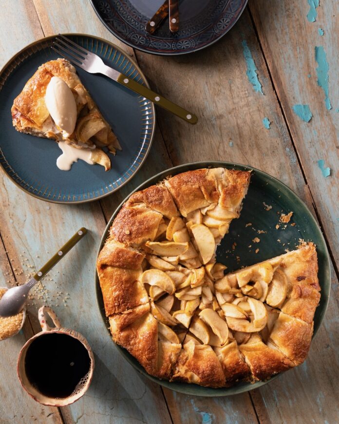On a dark plate sits an Apple Crostada inspired by Martha Stewart which is made with a cheddar cheese crust. One slice has been cut out and sits on another plate with a scoop of ice cream on top.