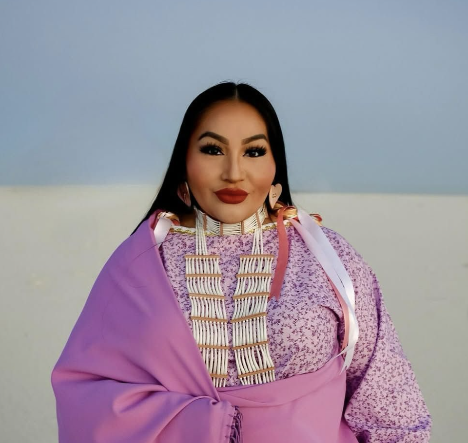 A woman in pink native fashion stands in front of a dessert backdrop.