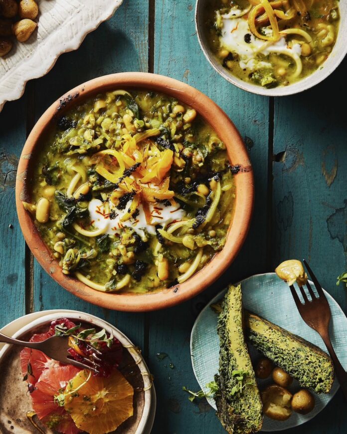 Persian Noodle Soup A Persian Noodle Soup sits in a brown bowl on a blue picnic table with three smaller bowls and plates of Persian food sitting around the soup.
