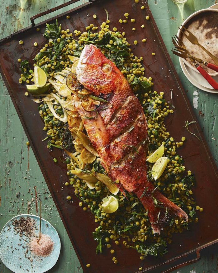 Red Snapper and Green Split Pea Salad for Holi TABLE Magazine A large Red Snapper lays on a cooking sheet surrounded by a Green Spit Pea Salad and limes in celebration of Nowruz.