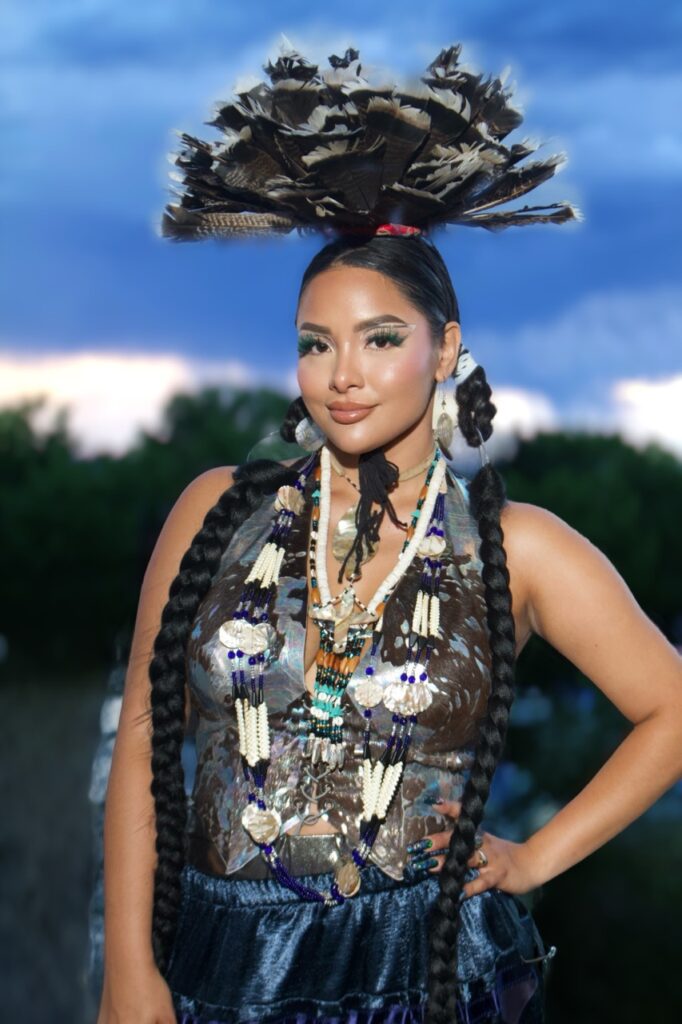 A woman in glitzy glam native wear with plenty of jewelry and a large headpiece.