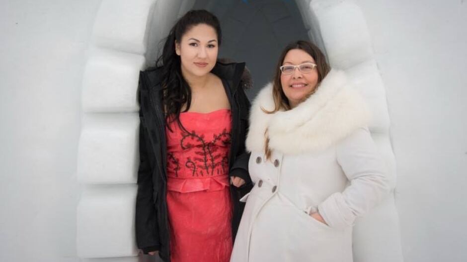 A woman in a pink dress and black fur coat stands next to a woman in a white fur coat.