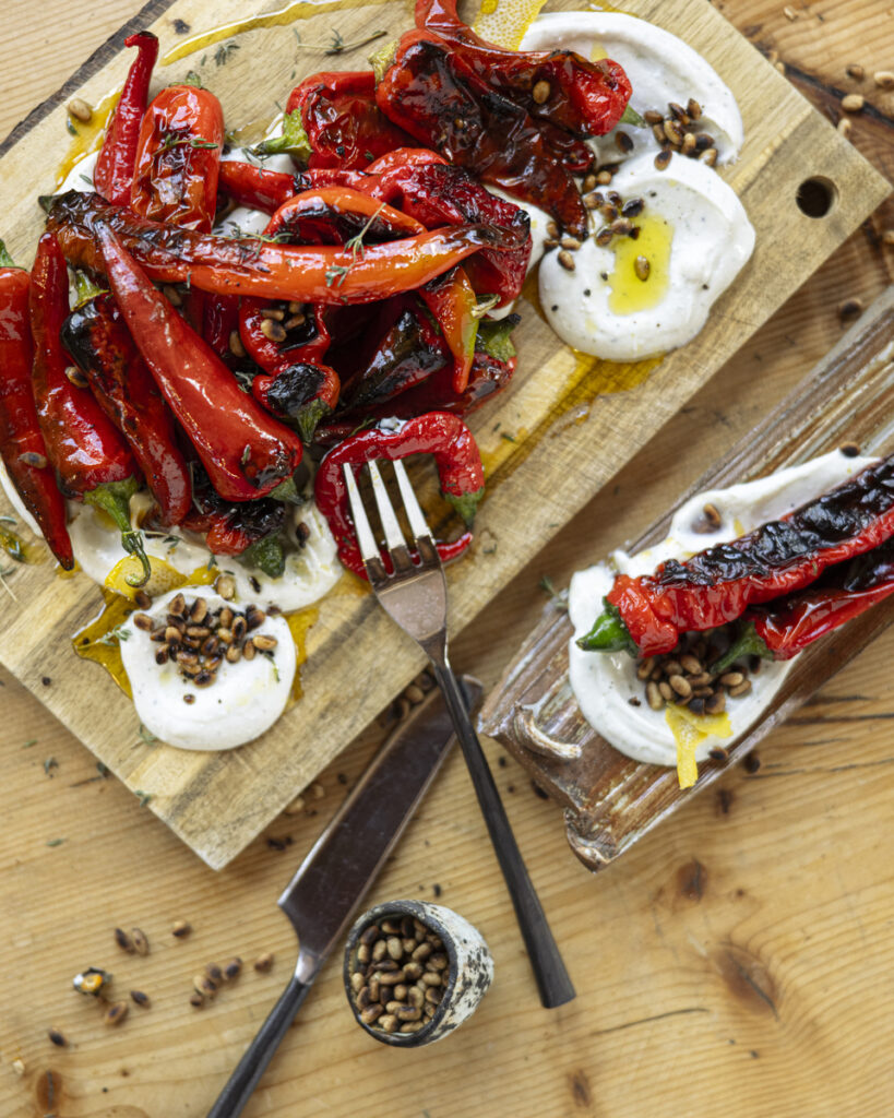 A dish features a swirl of creamy white labneh topped with pan-seared Jimmy Nardello and Lipstick peppers and a generous sprinkling of toasted pine nuts.