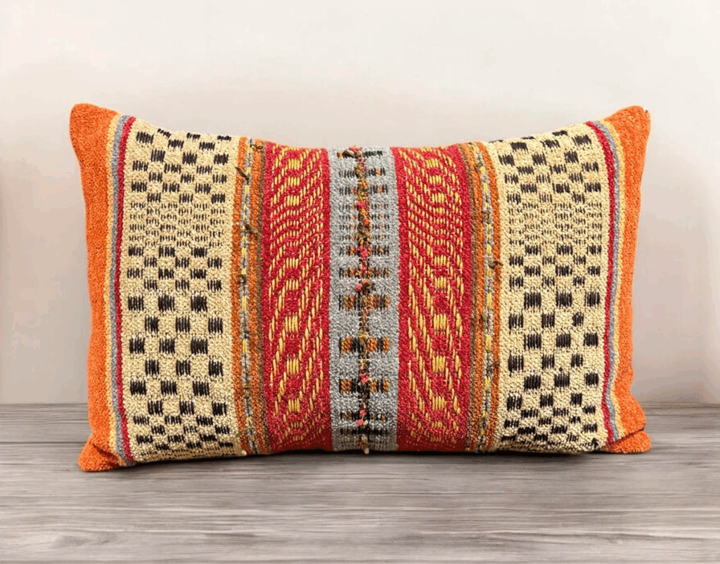 A rectangular throw pillow with a vibrant, woven pattern in orange, red, beige, and gray.