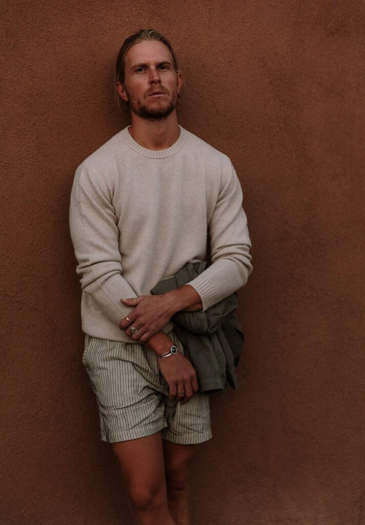 A fair-skinned man models a cream-colored sweater and striped shorts
