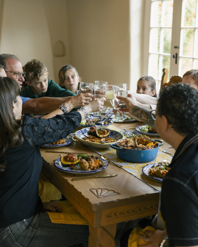 A multi-generational family of artists gathered around a table, sharing a meal and discussing New Mexico's artistic traditions.
