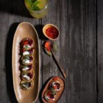 Buckwheat Blini served on a long plate with jam as a topping with a drink and a spoon on the side