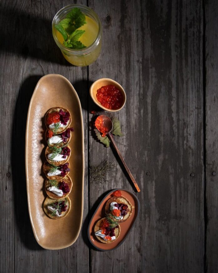 Buckwheat Blini served on a long plate with jam as a topping with a drink and a spoon on the side