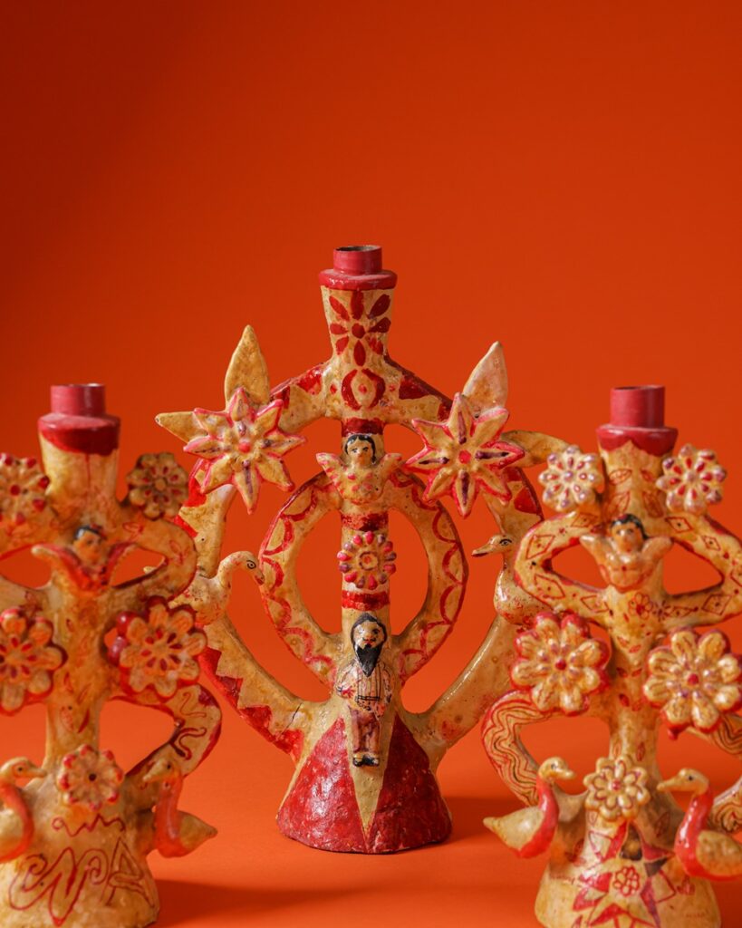 Three decorative ceramic candlesticks, primarily in warm tones of yellow and red, are arranged on an orange background.