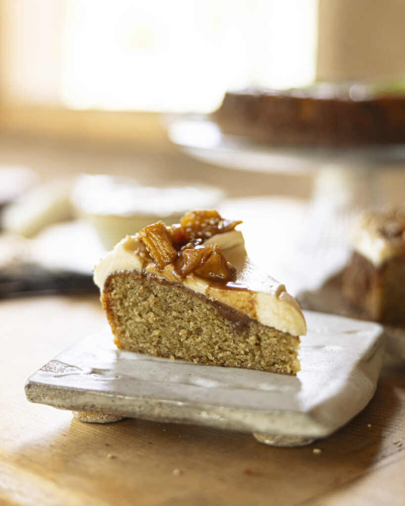 A light-colored olive oil cake with a dusting of powdered sugar is topped with a dollop of frosting.