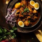 A bowl of Doro Wat, a rich Ethiopian chicken stew, with chicken pieces, hard-boiled eggs, and a thick, dark red sauce.