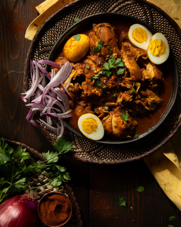 A bowl of Doro Wat, a rich Ethiopian chicken stew, with chicken pieces, hard-boiled eggs, and a thick, dark red sauce.