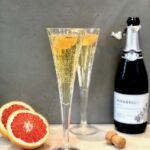 A Greyhound 75, two small glasses with a grapefruit and a Prosecco bottle beside it.