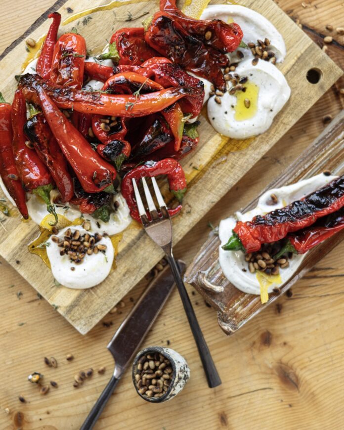 Harvest Mix Peppers TABLE Magazine A scorched harvest mix of peppers sit on a cutting board with labneh smeared beside them and herbs sprinkled over top.