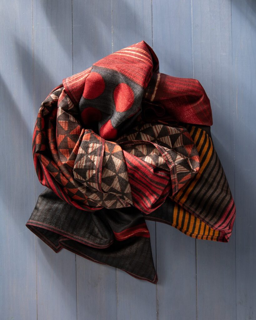 A richly patterned scarf with stripes, dots, and geometric designs in shades of red, black, orange, and beige, block printed on tussah silk.