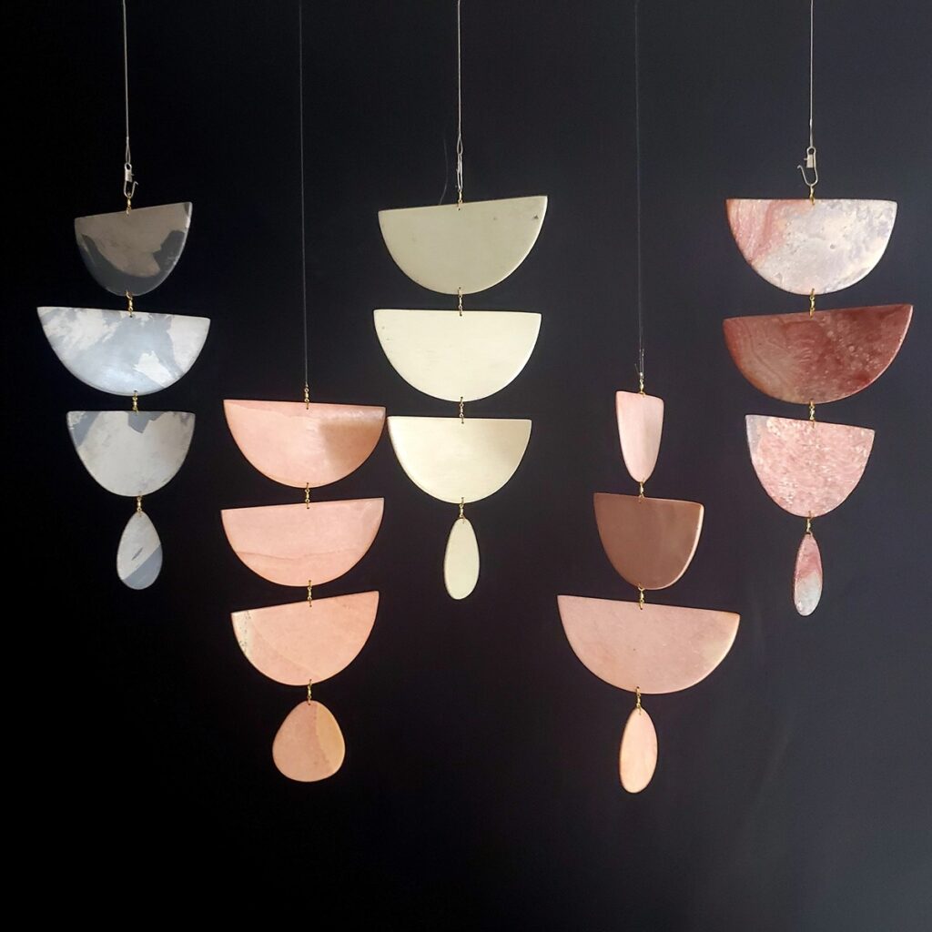 A Floc Parade mobile, handcrafted in Kenya from naturally-colored soapstone, featuring multiple hanging elements of three connected half circles and a teardrop shape at the end, against a dark background.