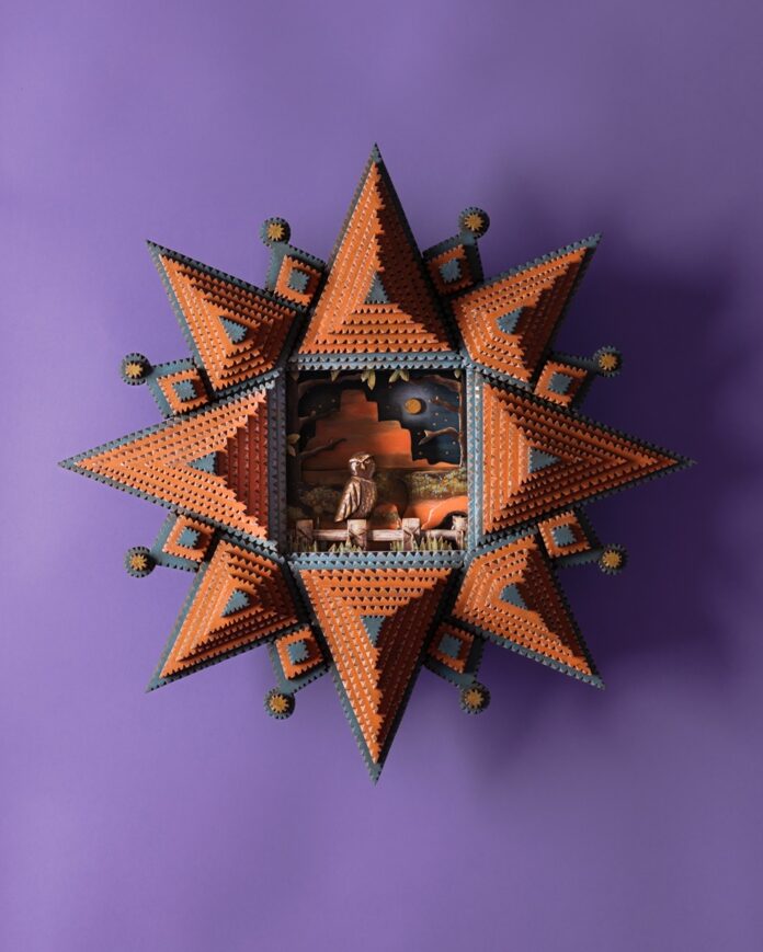 A vibrant, star-shaped tramp art piece in shades of orange and blue, with a detailed diorama in its center depicting a burrowing owl in a desert landscape under a moonlit sky.