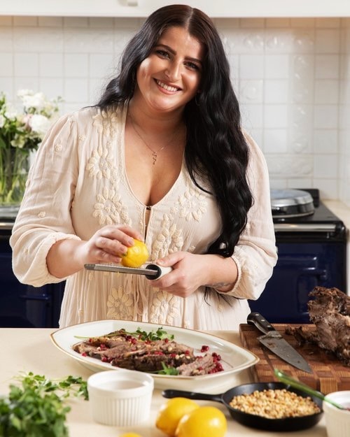 Lisa Theuer stands in front of her Pomegranate Molasses Roasted Lamb Shoulder in a white-walled kitchen.