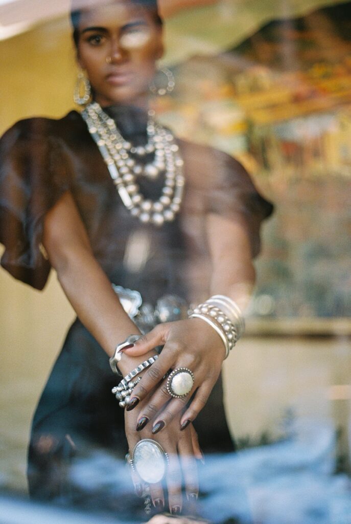 A woman, models multiple pieces of silver jewelry from Peyote Bird, including large rings, stacked bracelets, a concho belt, and layered necklaces and earrings.