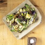 A stone rectangular plate holds a Roasted Cabbage Salad on a wood table beside a container of salt.